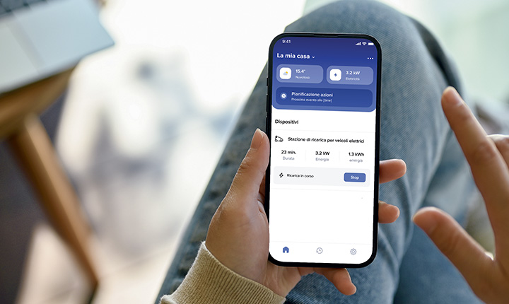 Persona con in mano uno smartphone con l'app schermata Home + Control in italiano, che gestisce i dispositivi e l'utilizzo dell'energia.