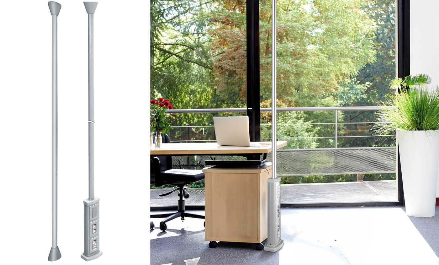 Un palo di alimentazione BT Colonne monofacciali con prese di corrente è installato accanto a una scrivania in un ufficio moderno con grandi finestre.