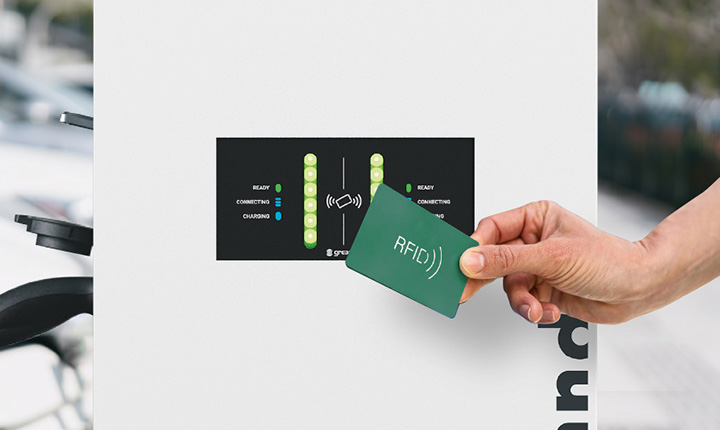 Una mano tiene una scheda RFID vicino a una colonnina di ricarica Green Up Control con indicatori luminosi.
