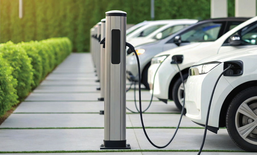 Fila di auto elettriche in ricarica presso le stazioni di ricarica all'aperto accanto a una siepe verde in una giornata di sole.