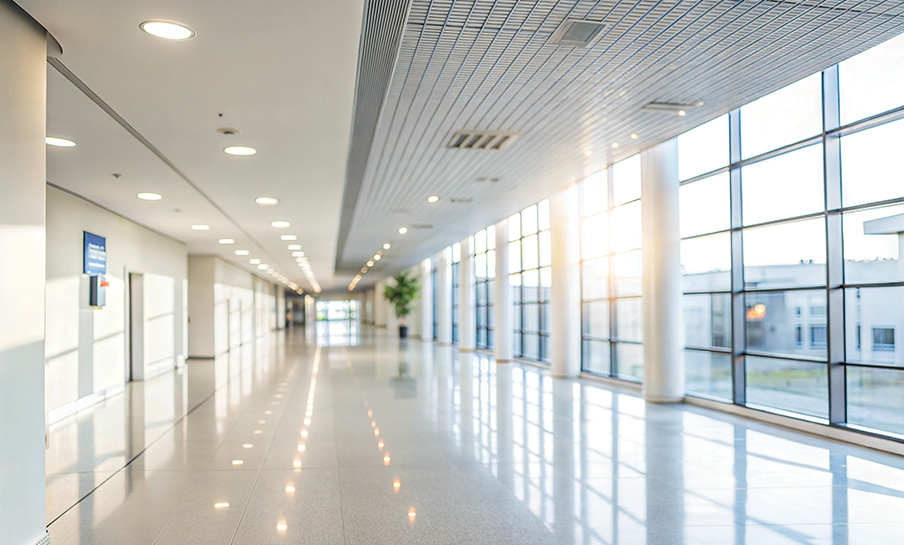 Un corridoio moderno e vuoto, con grandi finestre a tutta altezza e pavimenti lucidi, illuminato da luce naturale e artificiale.