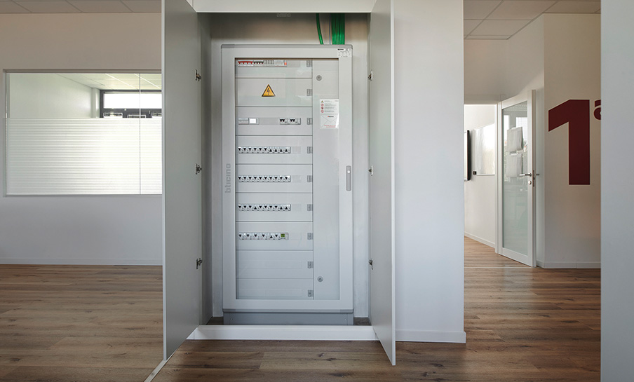 Quadro elettrico con interruttori BTicino e misuratori IME aperto in un corridoio di una scuola.
